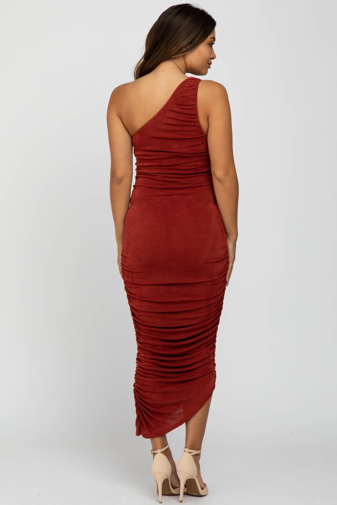 woman wearing a rust one-shoulder maternity dress with ruching details and a fitted silhouette