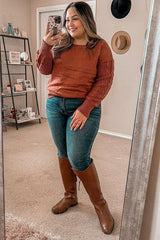 woman in rust orange cable knit sweater, blue jeans, and brown leather riding boots taking a mirror selfie