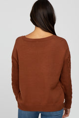 woman wearing a rust-colored sweater with cable-knit sleeves and a relaxed fit, view from the back