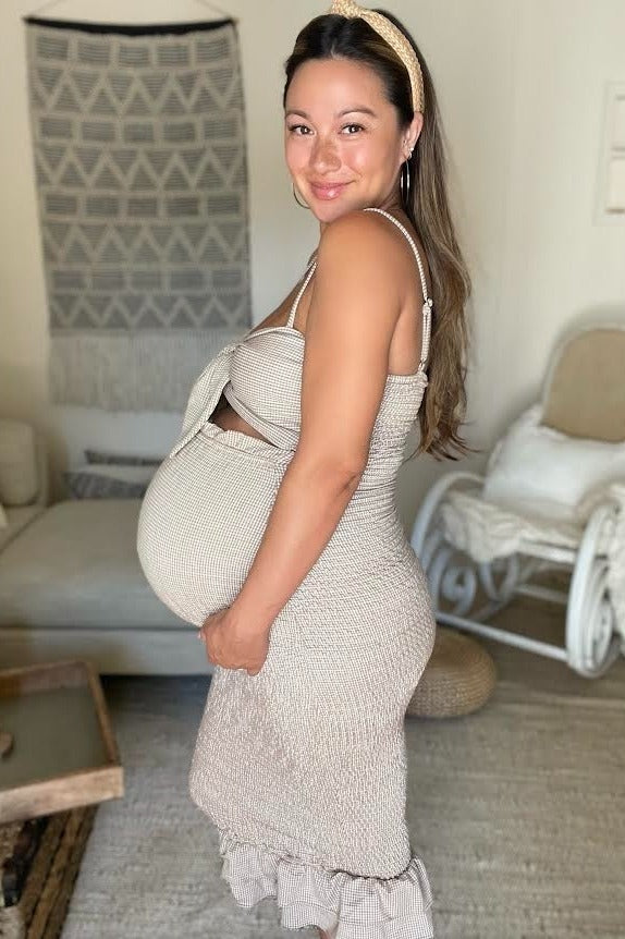 woman wearing a beige ribbed maternity dress with ruffle hem, smiling and showcasing her baby bump