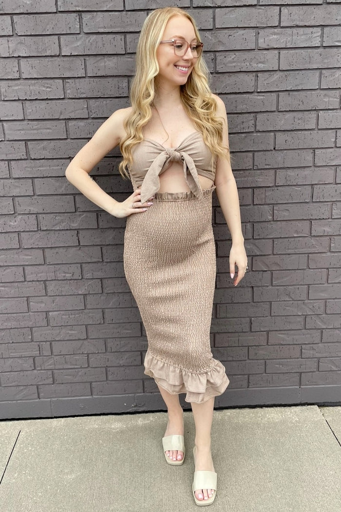 woman wearing a beige maternity dress with a knotted top and ruffled hem, displaying a visible baby bump
