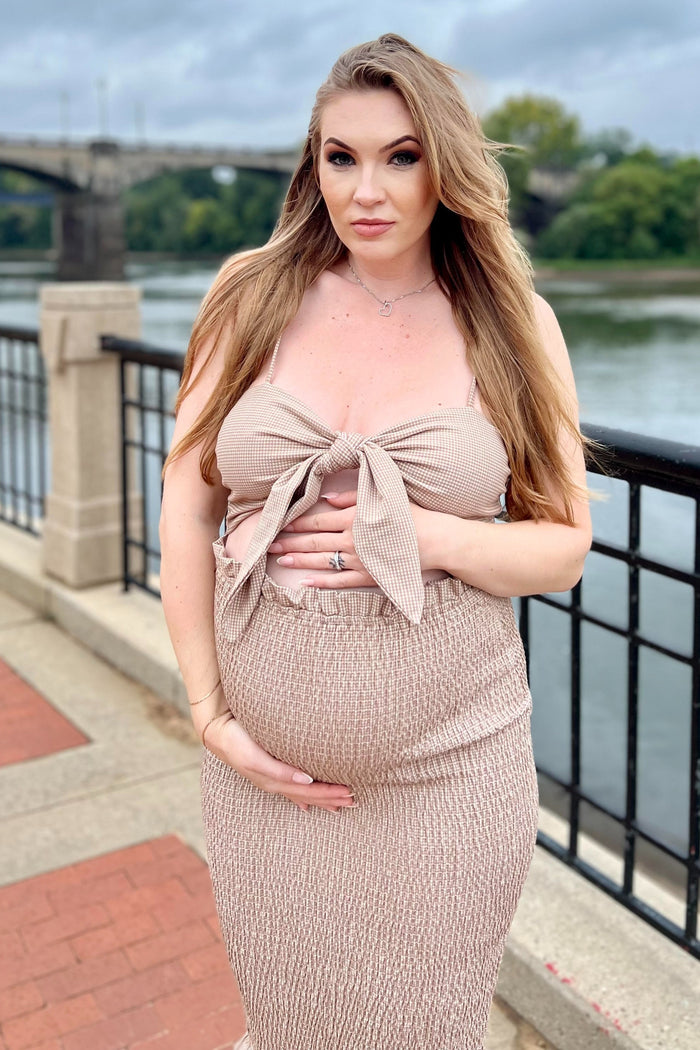 woman wearing a beige maternity two-piece dress with a knotted top and fitted skirt, holding her baby bump