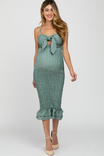 woman wearing a green smocked maternity dress with a tie front and ruffle hem, showcasing her baby bump