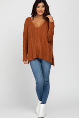 woman wearing an oversized rust cable knit sweater with a v-neck and side splits, paired with skinny jeans and ankle boots