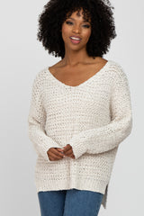 woman wearing a cream v-neck knitted sweater with a loose fit and long sleeves, paired with blue jeans