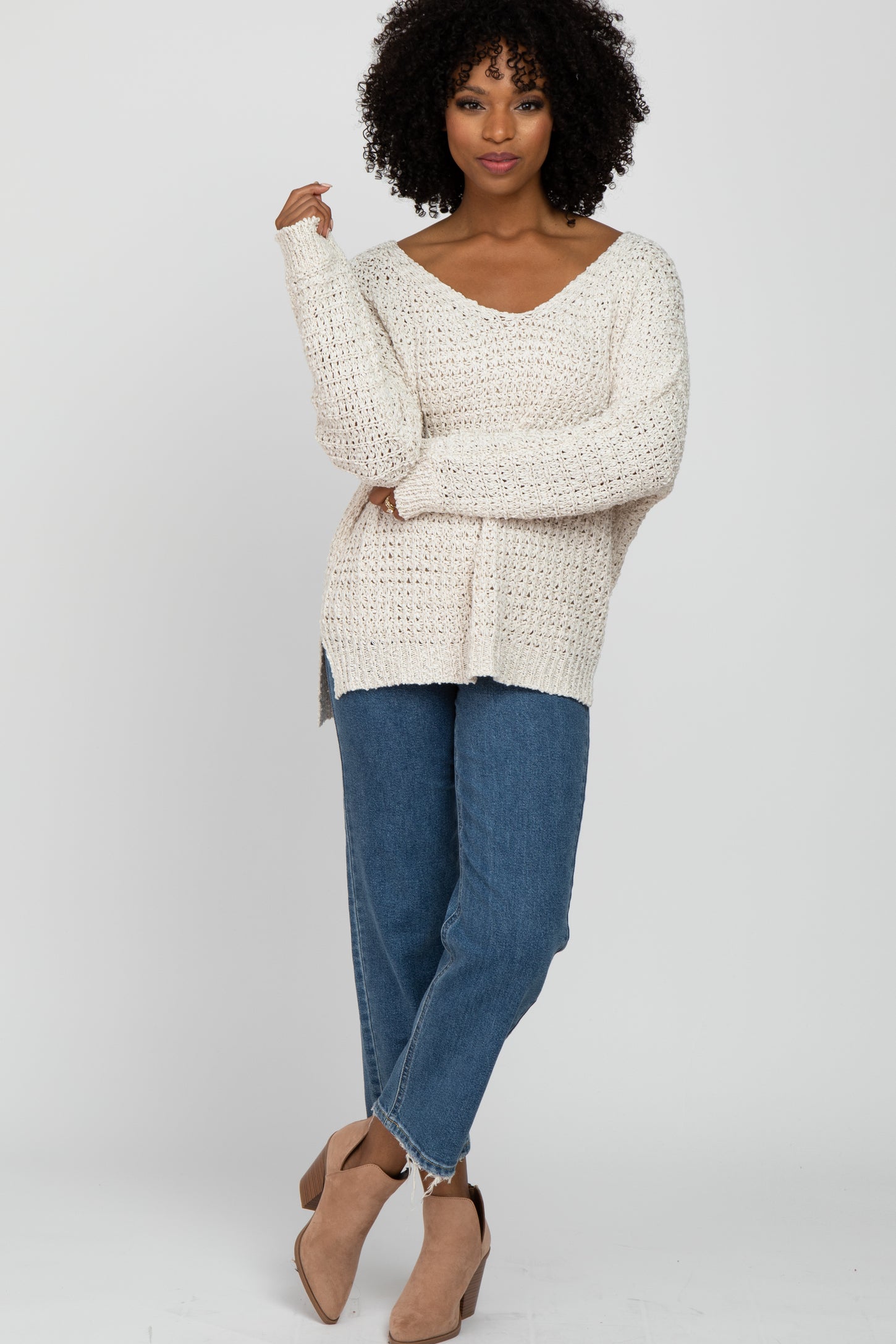 woman wearing a cream oversized knit sweater with a v-neck and side slits, paired with light blue loose-fit jeans and ankle boots