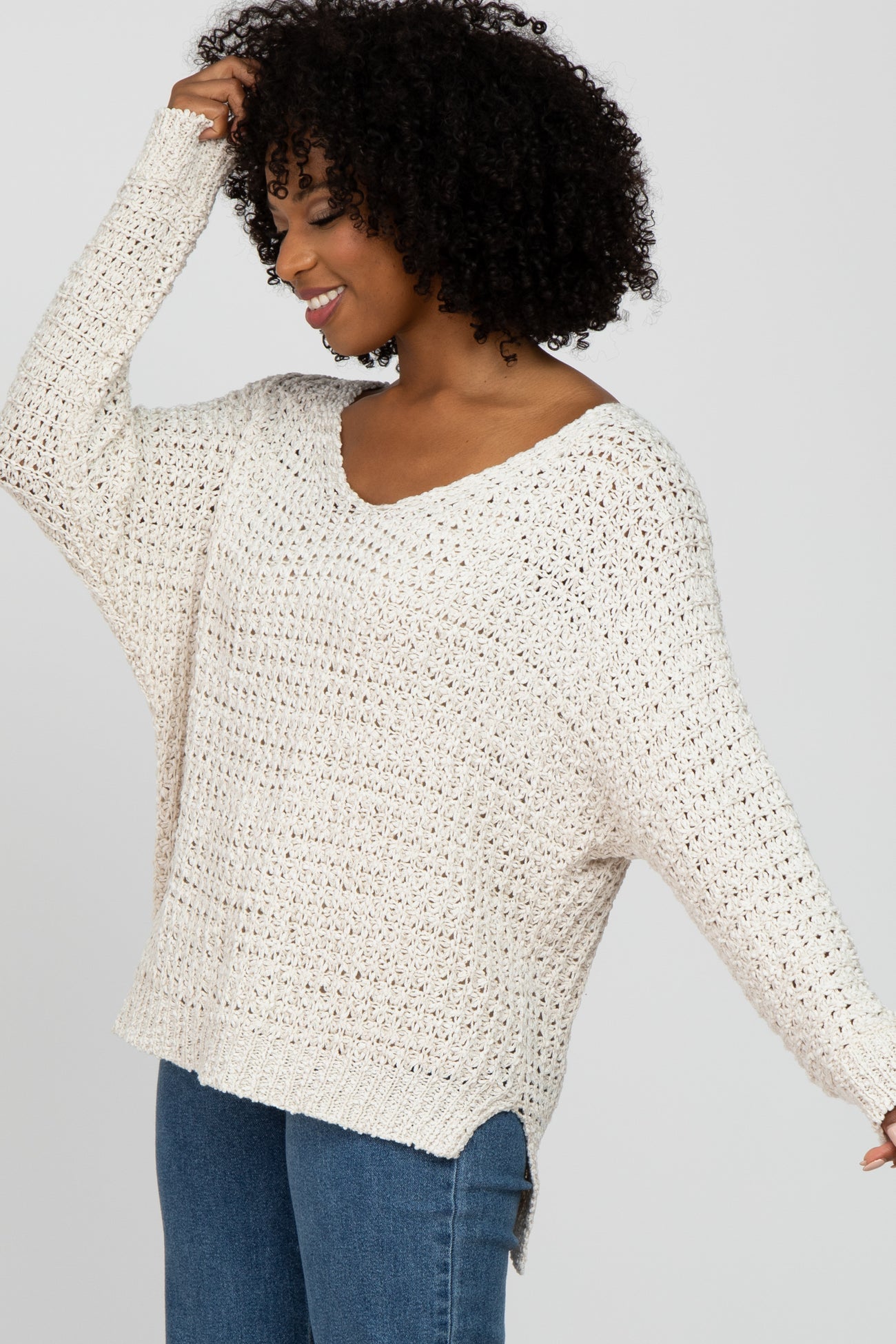 woman wearing a beige crochet sweater with a v-neck and side slits, styled casually with blue jeans