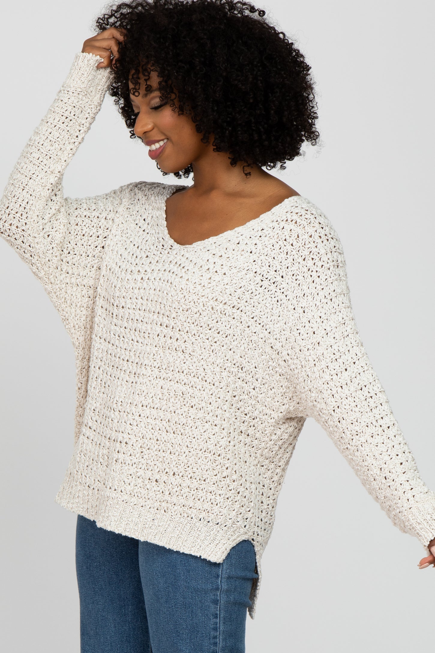woman wearing a beige crochet sweater with a v-neck and side slits, styled casually with blue jeans