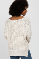 woman wearing a light beige open knit sweater with a loose fit and side slits, paired with blue jeans
