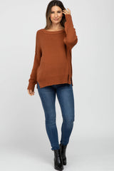 woman wearing a rust-colored oversized ribbed maternity sweater with side slits paired with skinny jeans