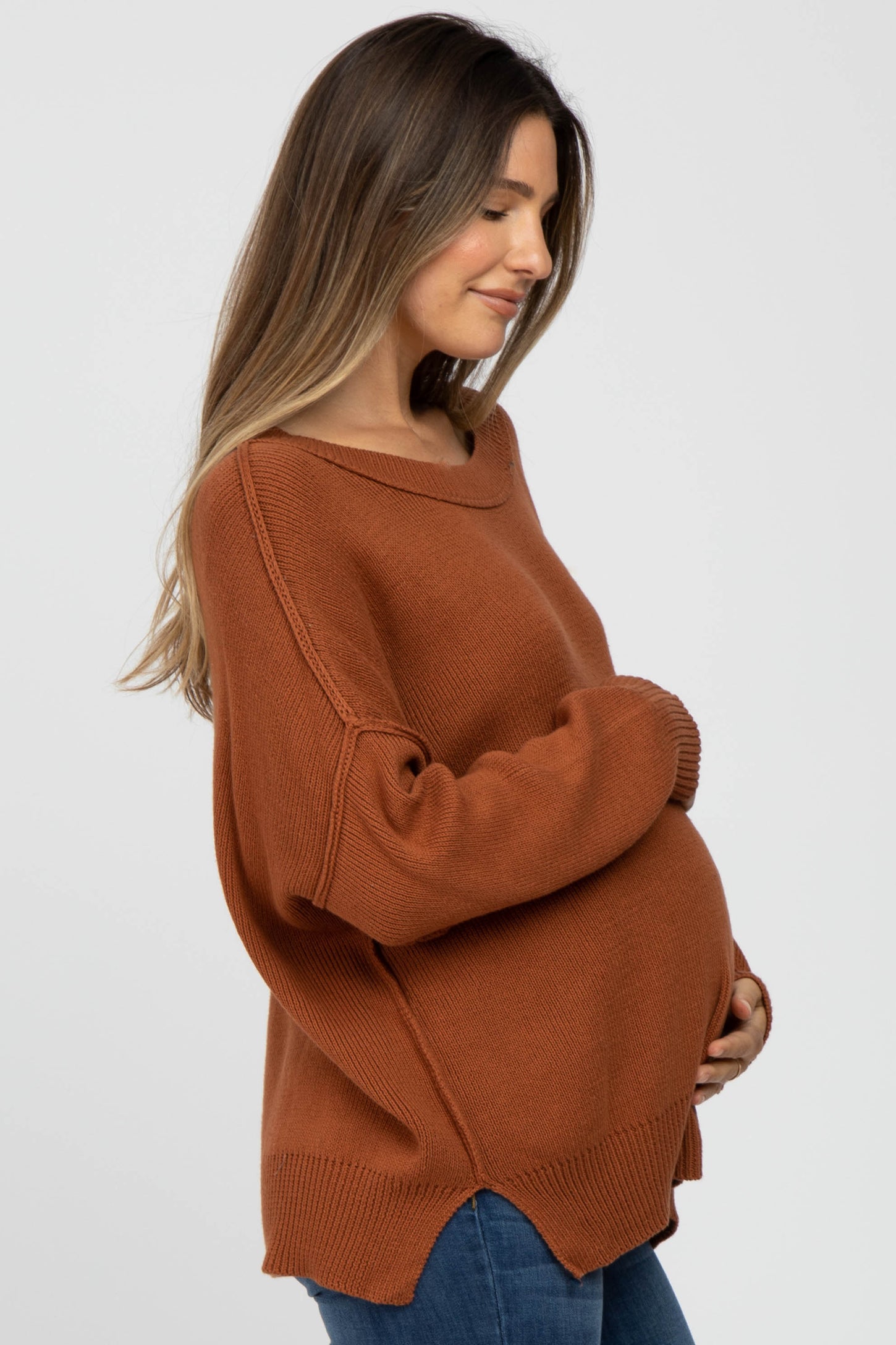 woman wearing a rust-colored oversized maternity sweater and gently cradling her baby bump