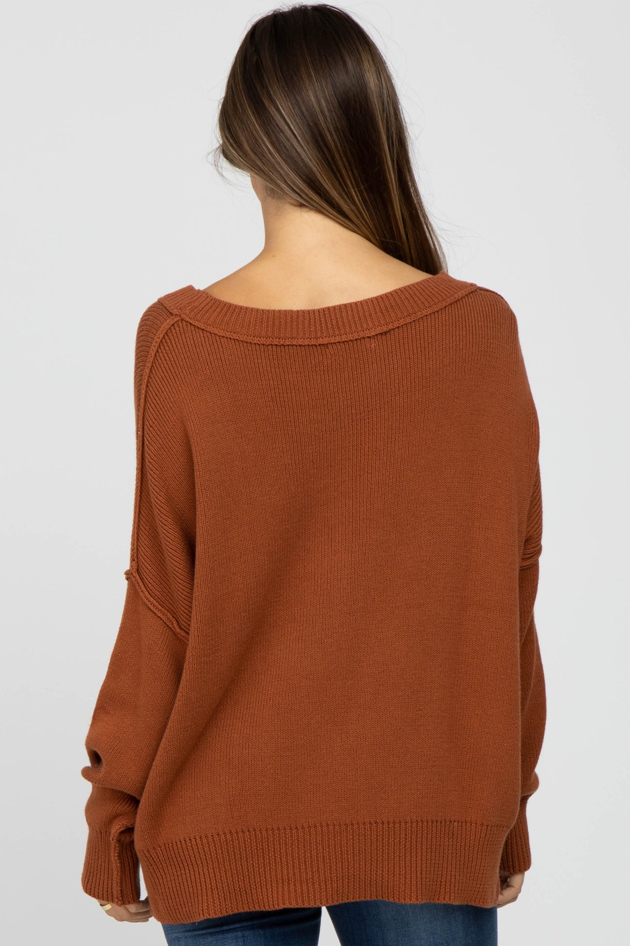 woman wearing a rust-colored oversized maternity sweater with a wide neckline and relaxed fit