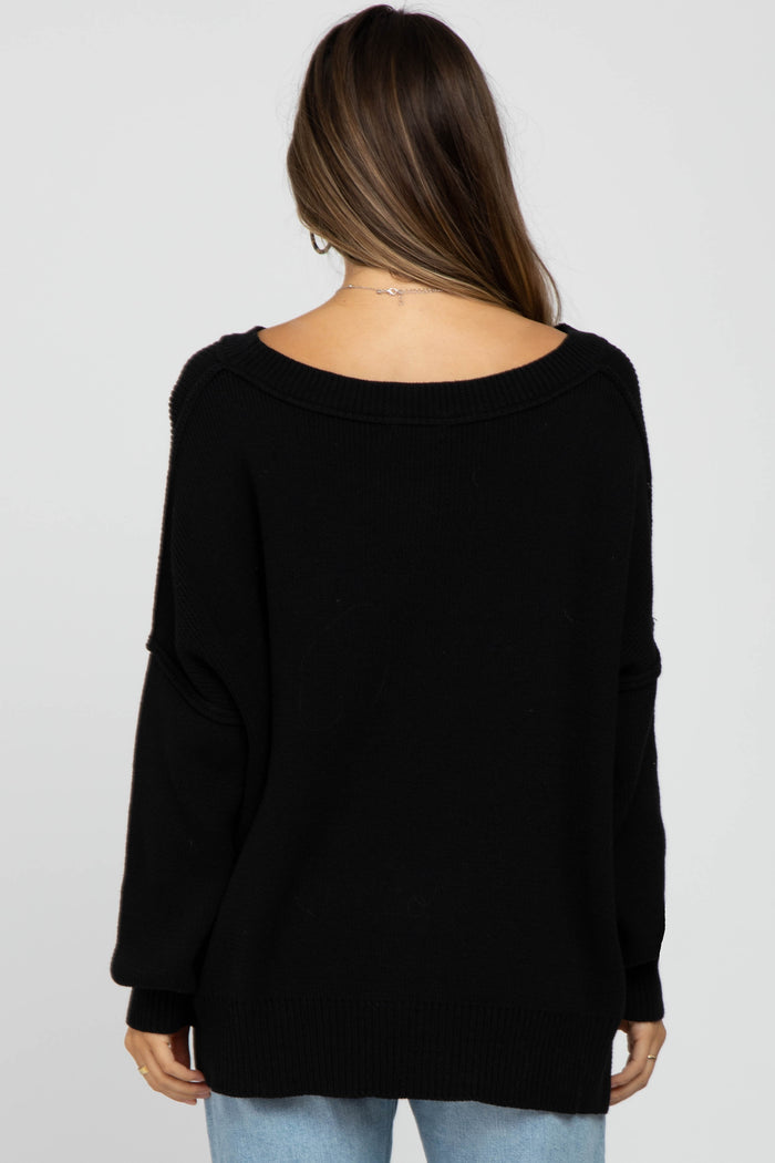 Back view of a woman wearing an oversized black knit sweater with a wide neckline and long sleeves