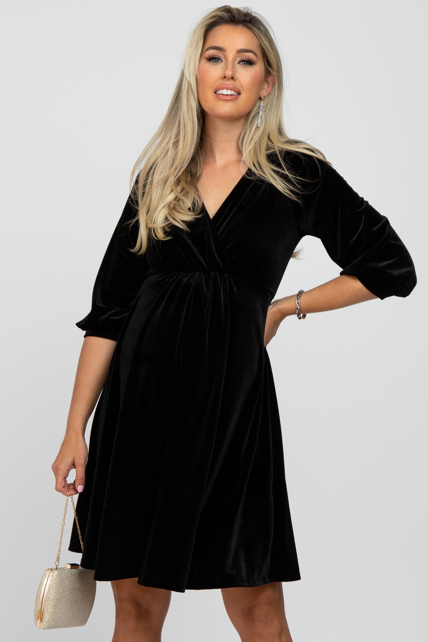 woman wearing a black velvet maternity dress with three-quarter sleeves and holding a small clutch bag