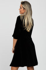 woman wearing a black velvet maternity dress with three-quarter sleeves looking over her shoulder