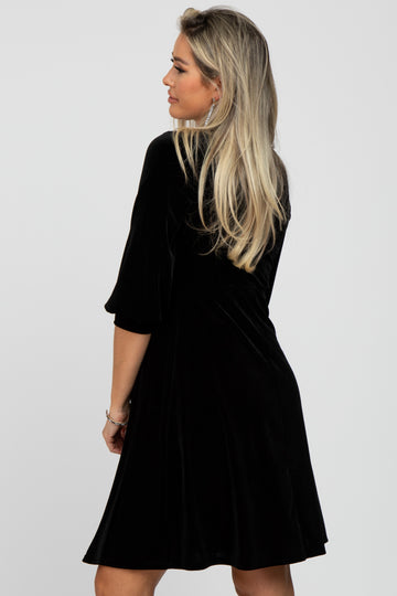 woman wearing a black velvet maternity dress with three-quarter sleeves looking over her shoulder