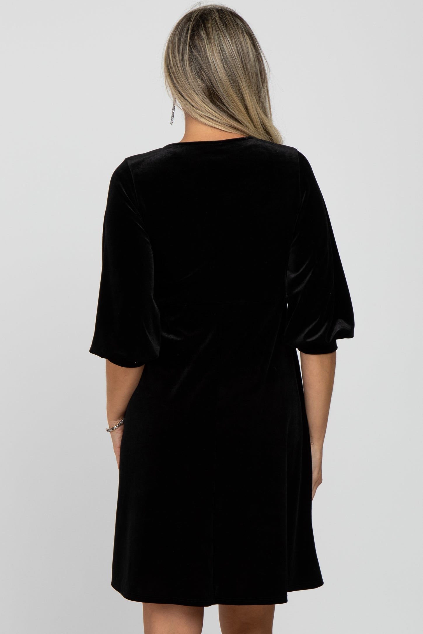 woman wearing a black velvet maternity dress with short puff sleeves, showing the back view