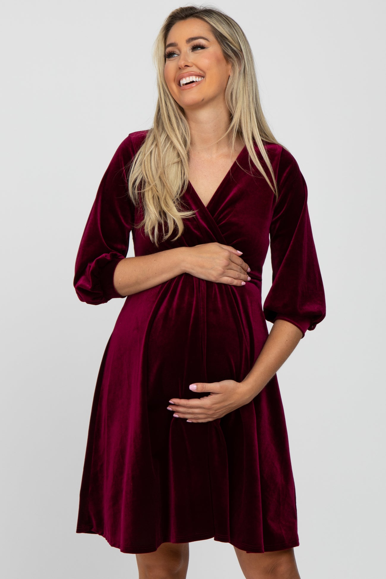 smiling pregnant woman in a burgundy velvet wrap maternity dress with three-quarter sleeves