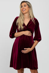 smiling pregnant woman in a burgundy velvet wrap maternity dress with three-quarter sleeves