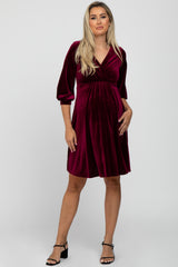 woman wearing a burgundy velvet maternity dress with a v-neck and three-quarter sleeves, holding her baby bump