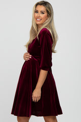 woman wearing a burgundy velvet maternity dress, holding her baby bump with a smile