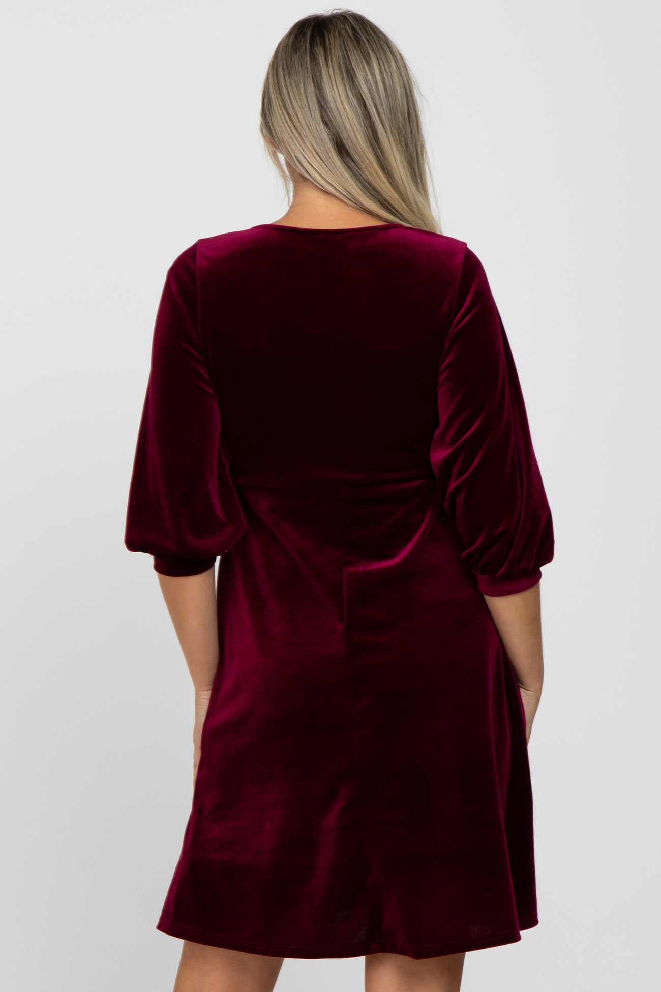 woman wearing a burgundy velvet maternity dress with puff sleeves and a relaxed fit from the back