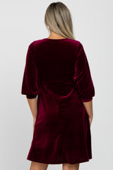 woman wearing a burgundy velvet maternity dress with puff sleeves and a relaxed fit from the back
