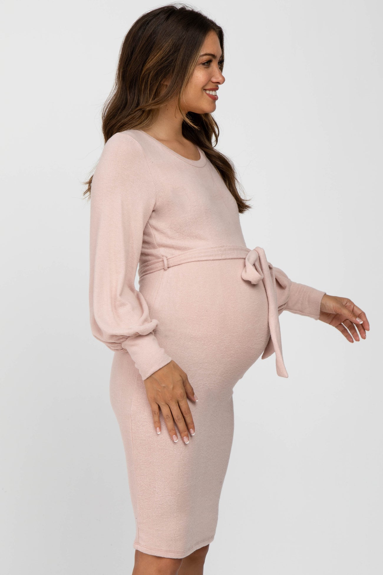 woman wearing a light pink long sleeve maternity dress with a tie detail at the waist and visible baby bump