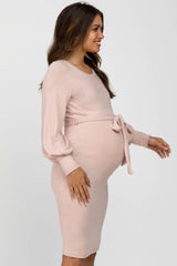 woman wearing a light pink long sleeve maternity dress with a tie detail at the waist and visible baby bump