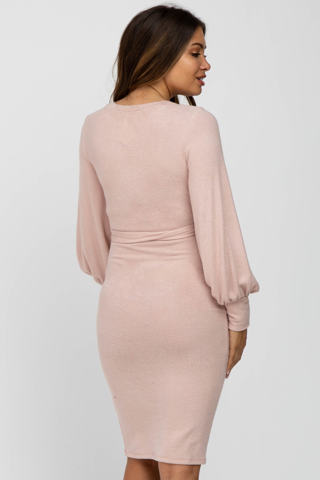 woman wearing a light pink long sleeve maternity dress with puff sleeves, showing a fitted silhouette from the back