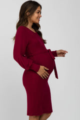 woman wearing a burgundy maternity dress with long sleeves and a tie waist, showing her baby bump