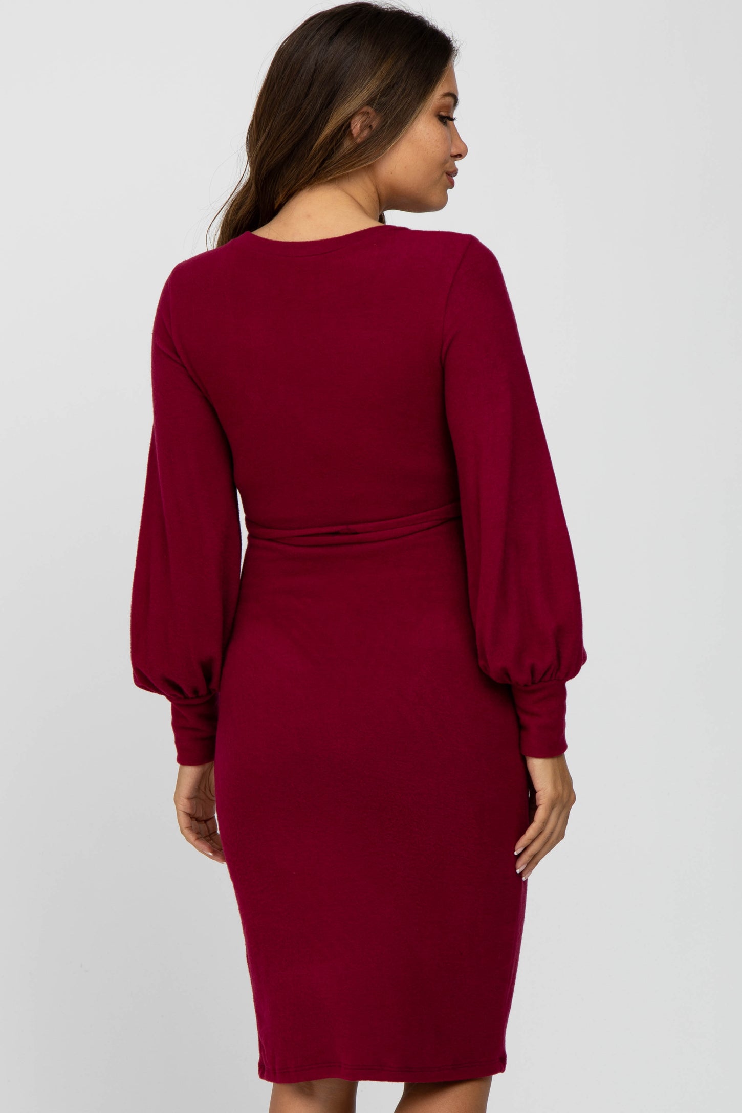 woman wearing a burgundy long sleeve maternity dress with puff sleeves, showcasing a fitted silhouette from the back