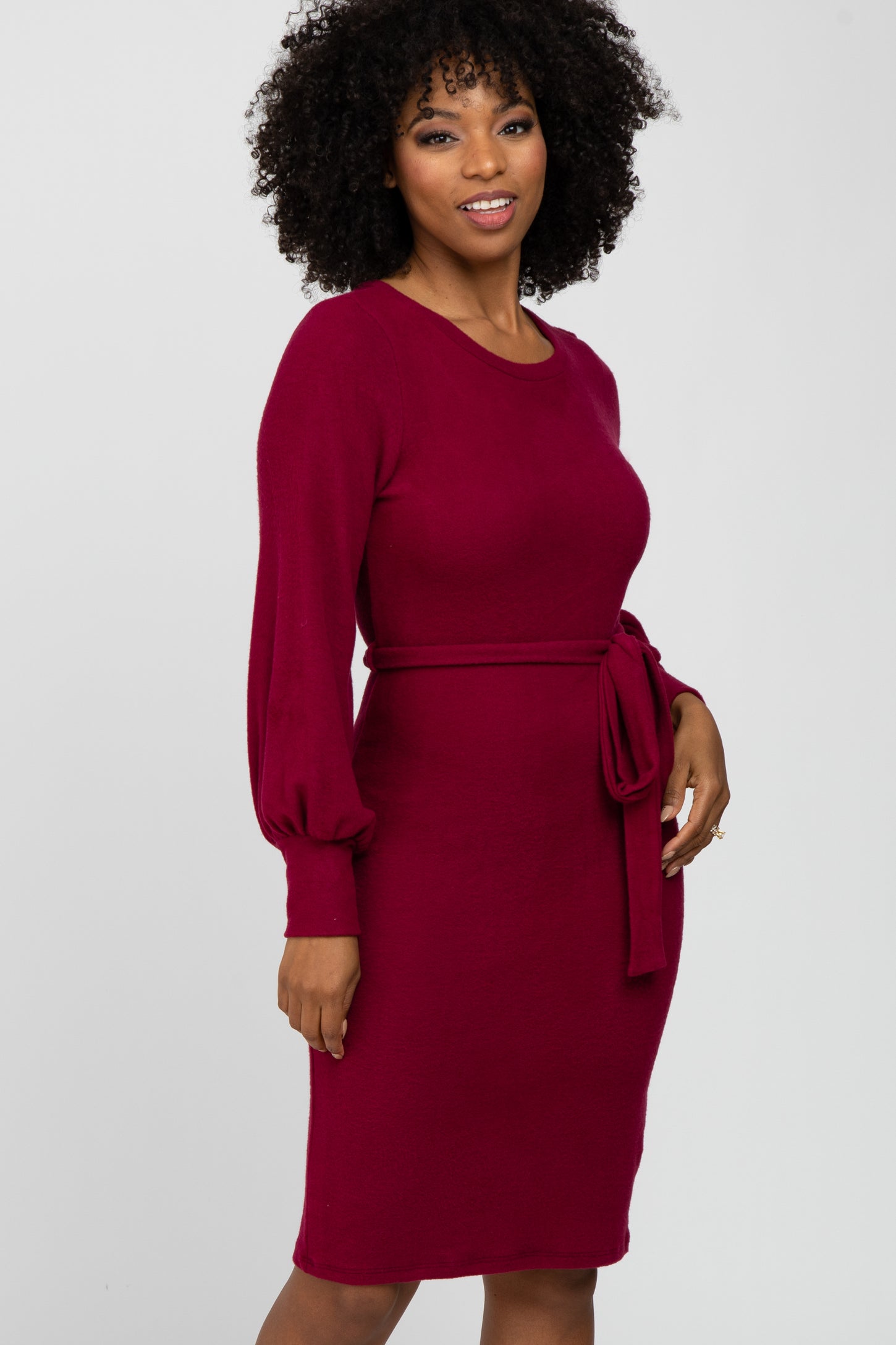 woman wearing a burgundy long sleeve dress with a tie belt at the waist and a fitted silhouette