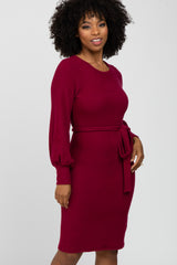 woman wearing a burgundy long sleeve dress with a tie belt at the waist and a fitted silhouette