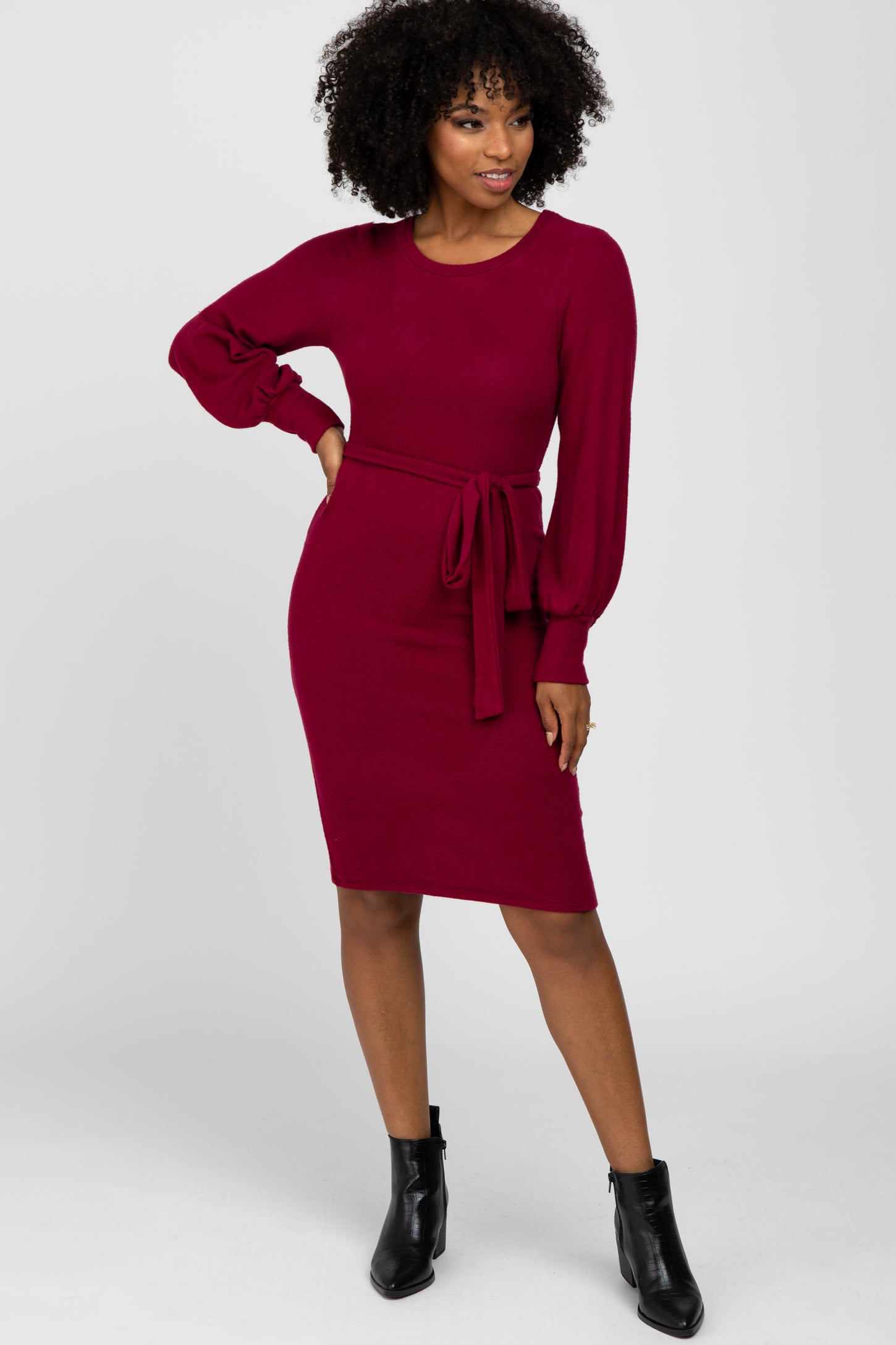 woman wearing a maroon long sleeve knit dress with a tie waist detail and black ankle boots