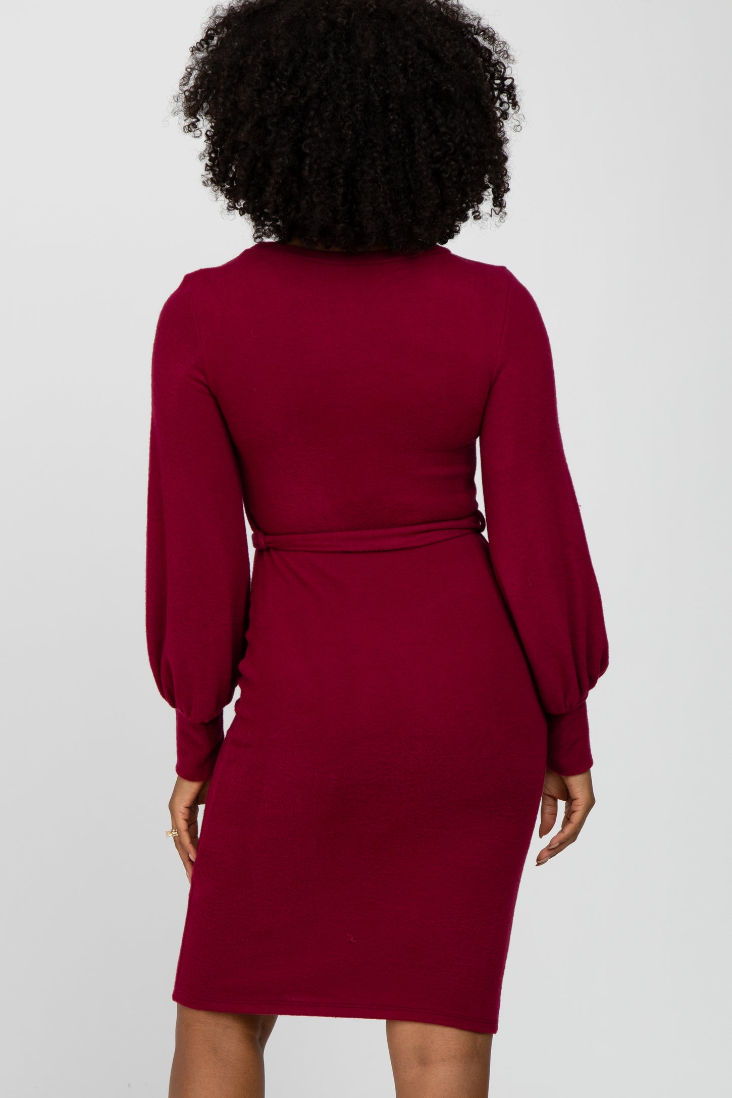 woman wearing a burgundy long sleeve dress with a fitted silhouette and puffed sleeves, shown from the back