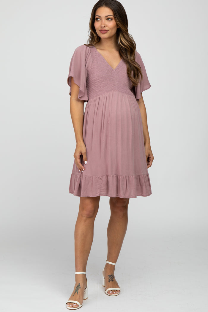 woman wearing a mauve maternity dress with flutter sleeves and a ruffled hem, showing her baby bump
