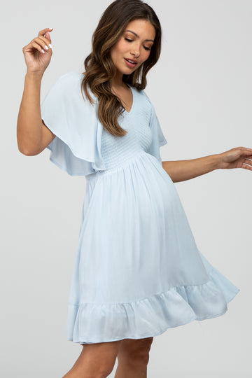 woman wearing a light blue flutter sleeve maternity dress with a smocked bodice and ruffled hem, showcasing her baby bump