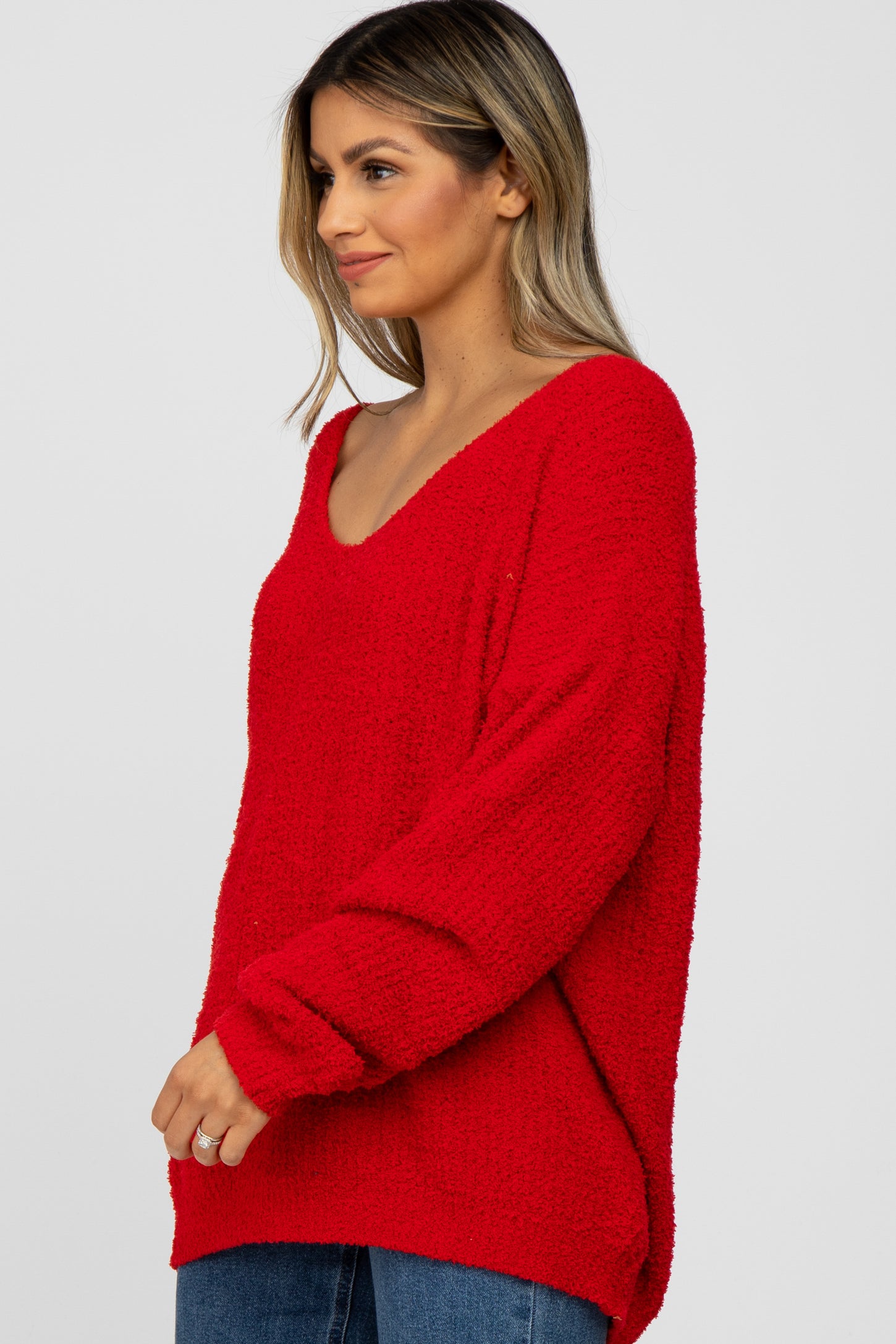 woman wearing a red cozy oversized sweater with a v-neck and long sleeves paired with blue jeans