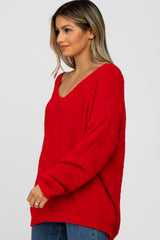 woman wearing a red cozy oversized sweater with a v-neck and long sleeves paired with blue jeans