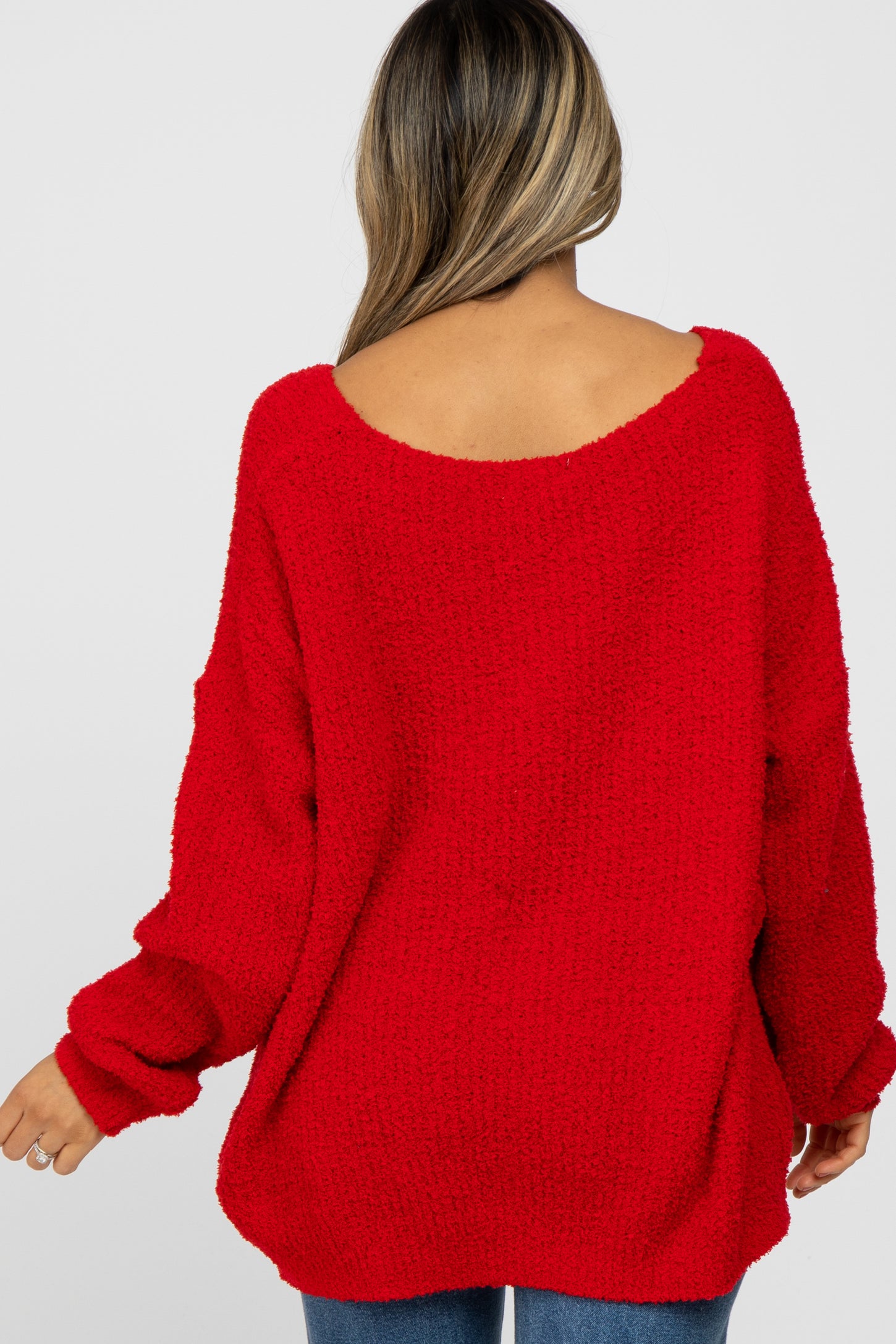 woman wearing a red oversized sweater with a wide neckline and long sleeves, viewed from the back