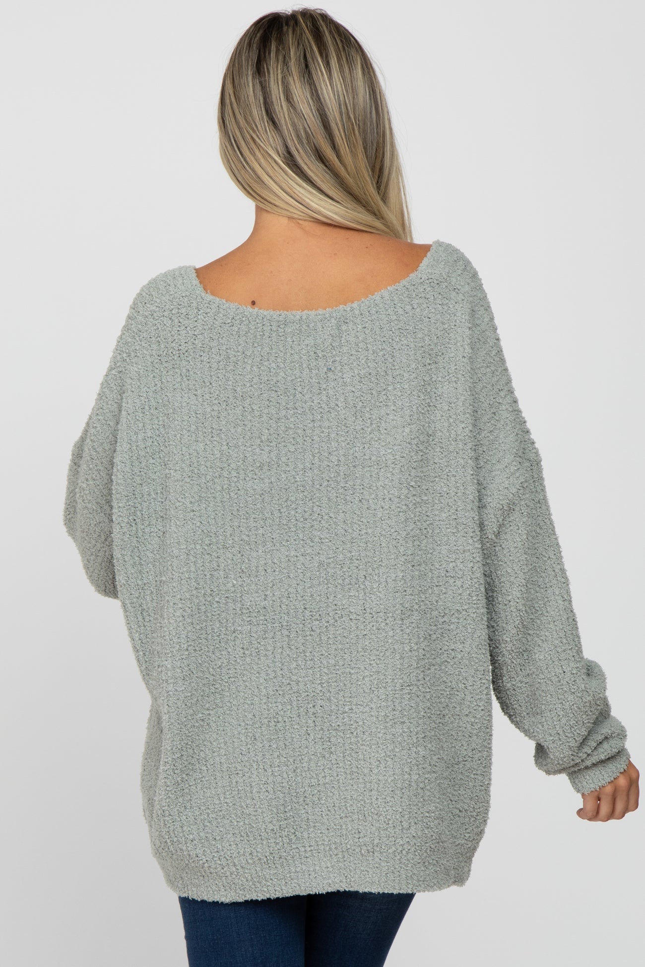 back view of a woman wearing an oversized light green fuzzy knit sweater and blue jeans