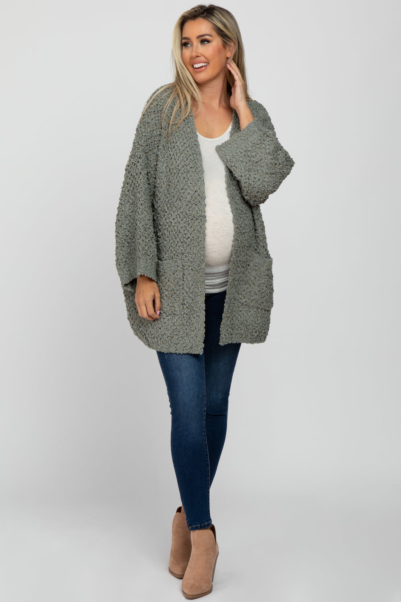 woman wearing a light grey maternity sweater over a white top and blue jeans, showing her baby bump
