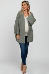 woman wearing a light grey maternity sweater over a white top and blue jeans, showing her baby bump
