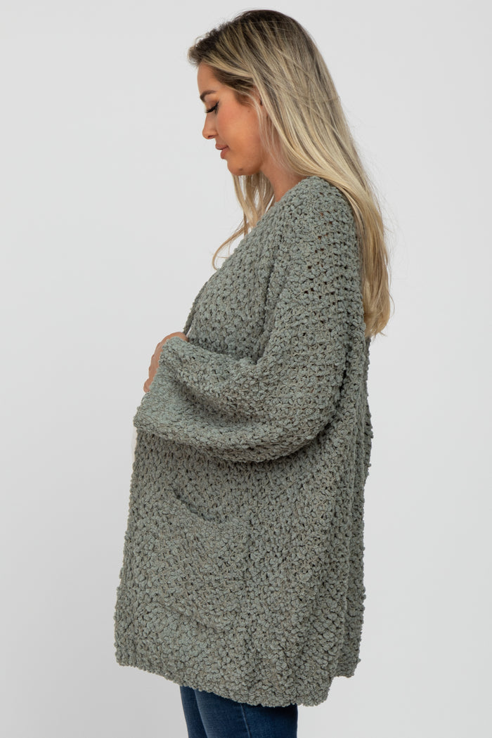 woman wearing a green crochet maternity cardigan and holding her baby bump