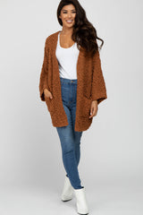 woman wearing a brown fuzzy open front cardigan over a white top and blue skinny jeans with white ankle boots