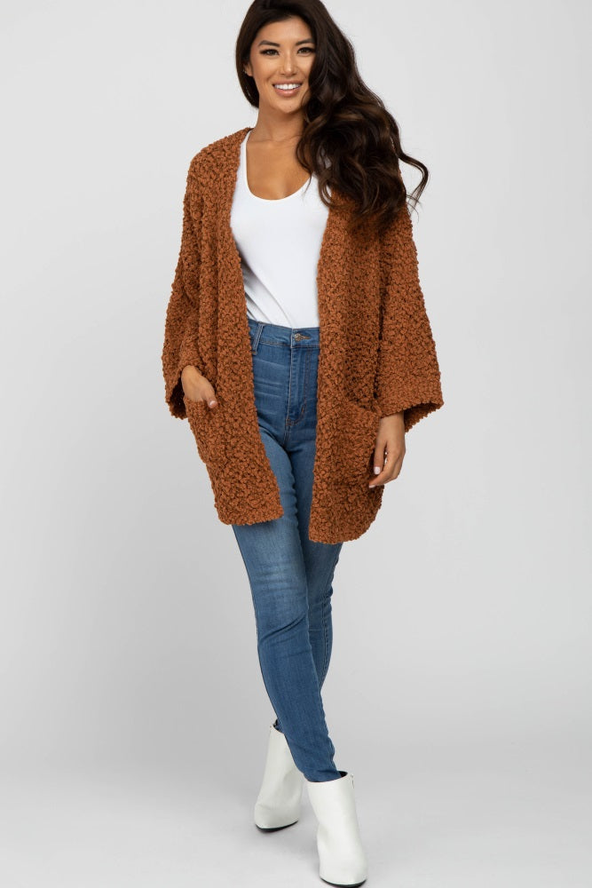 woman wearing a brown fuzzy open front cardigan over a white top and blue skinny jeans with white ankle boots