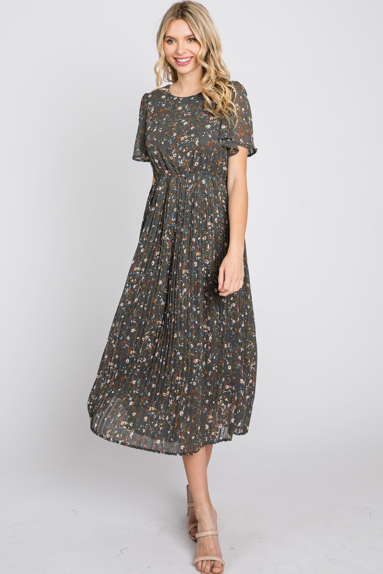 woman wearing a dark floral midi dress with short sleeves and a pleated skirt, smiling and standing in a relaxed pose