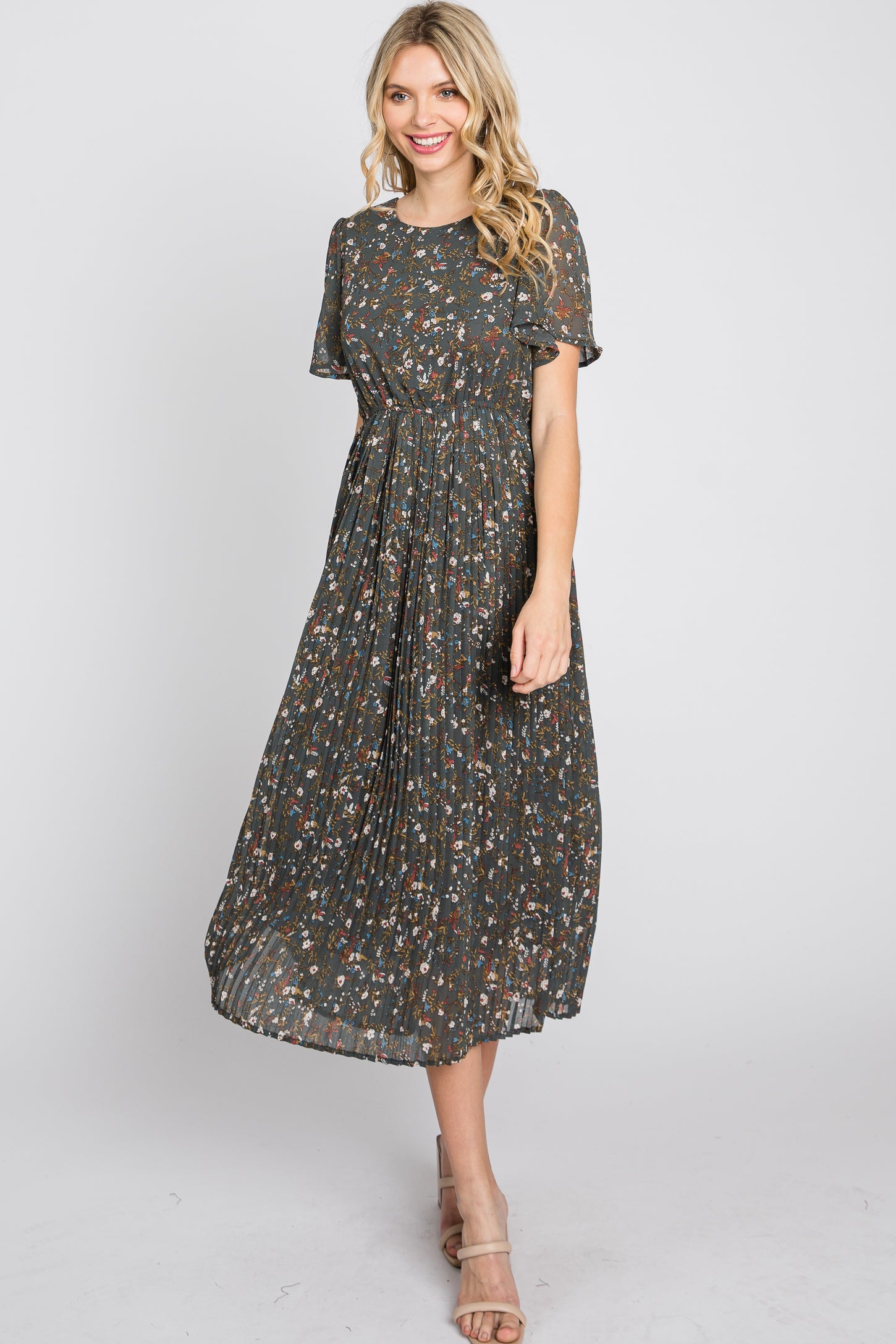 woman wearing a dark floral midi dress with short sleeves and a pleated skirt, smiling and standing in a relaxed pose