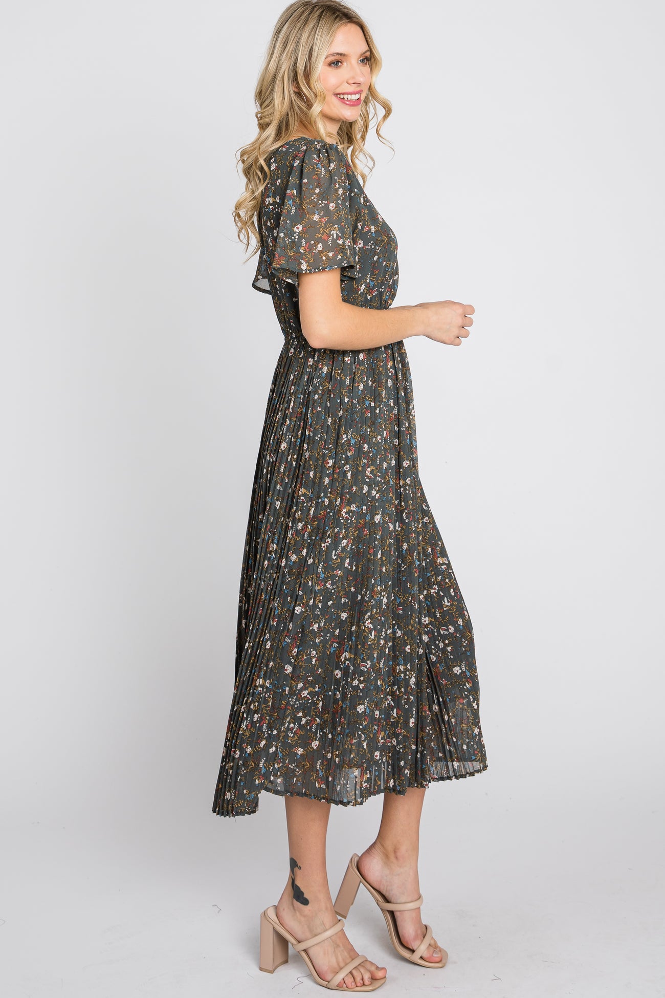 woman wearing a dark floral midi dress with short sleeves and pleated skirt, standing sideways with a smile